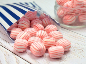 Pink and white striped soft crumbly sweet spilling out of a paper bag.