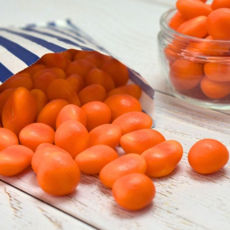 Orange butternuts sweets spilling from a blue and white striped paper bag.