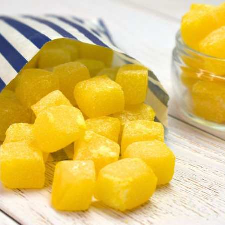 Yellow pineapple cube sweets spilling from a blue and white striped paper bag.