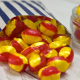 Red and yellow rhubarb and custard sweets spilling from a blue and white striped paper bag.
