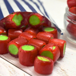 Red & Green Rhubarb rock sweets spilling from a blue and white striped paper bag.