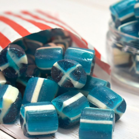 Blue and white saltire rock sweets, spilling from a red and white striped paper bag.