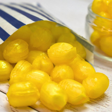 Yellow sherbet lemon sweets spilling from a blue and white striped paper bag.