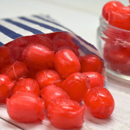 Red sherbet strawberry sweets spilling from a blue and white striped paper bag.