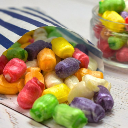 Rainbow colour sherbet straws sweets spilling from a blue and white striped paper bag.