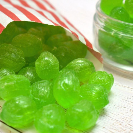 Green Soor Plooms sweets spilling from a red and white striped paper bag.