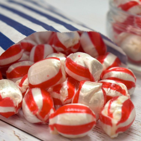 Red and white strawberry & cream sweets spilling from a blue and white striped paper bag.
