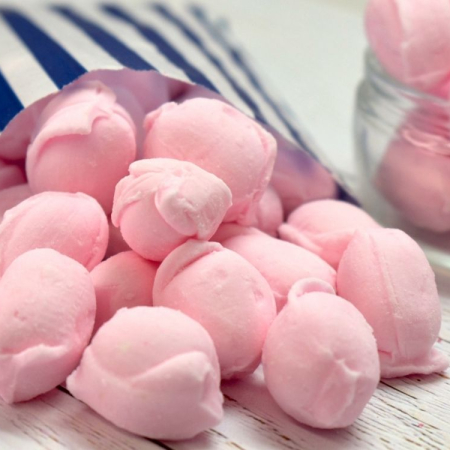 Pink, crumbly rose cream sweets spilling from a blue and white striped paper bag.