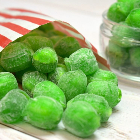 Green sherbet lime sweets spilling from a red and white striped paper bag.