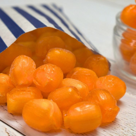 Orange sherbet orange sweets spilling from a blue and white striped paper bag.