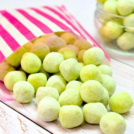 Light green chewy apple bonbons dusted in icing sugar spilling out of paper bag
