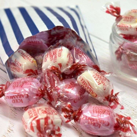 Pink and white Iced caramels sweets spilling from a blue and white striped paper bag.