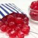 Red cherry drops sweets spilling from a blue and white striped paper bag.