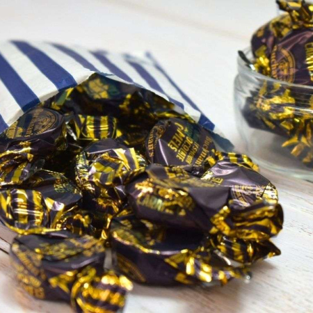 Gold-wrapped Buchanan's dark chocolate caramels spilling from a blue and white striped paper bag.