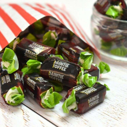 McCowans Daintie Toffees in maroon and green wrappers spilling from a red and white striped paper bag.