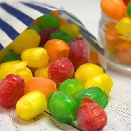 Colourful sherbet fruit sweets spilling from a blue and white striped paper bag.